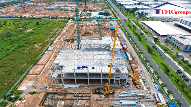 Aerial view of an industrial factory under construction in Vietnam, featuring structural steel installation, heavy lifting equipment and modern industrial infrastructure, presented by TTTFIC Group