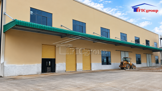 Industrial factory exterior with roller shutter doors, a green canopy and a concrete yard